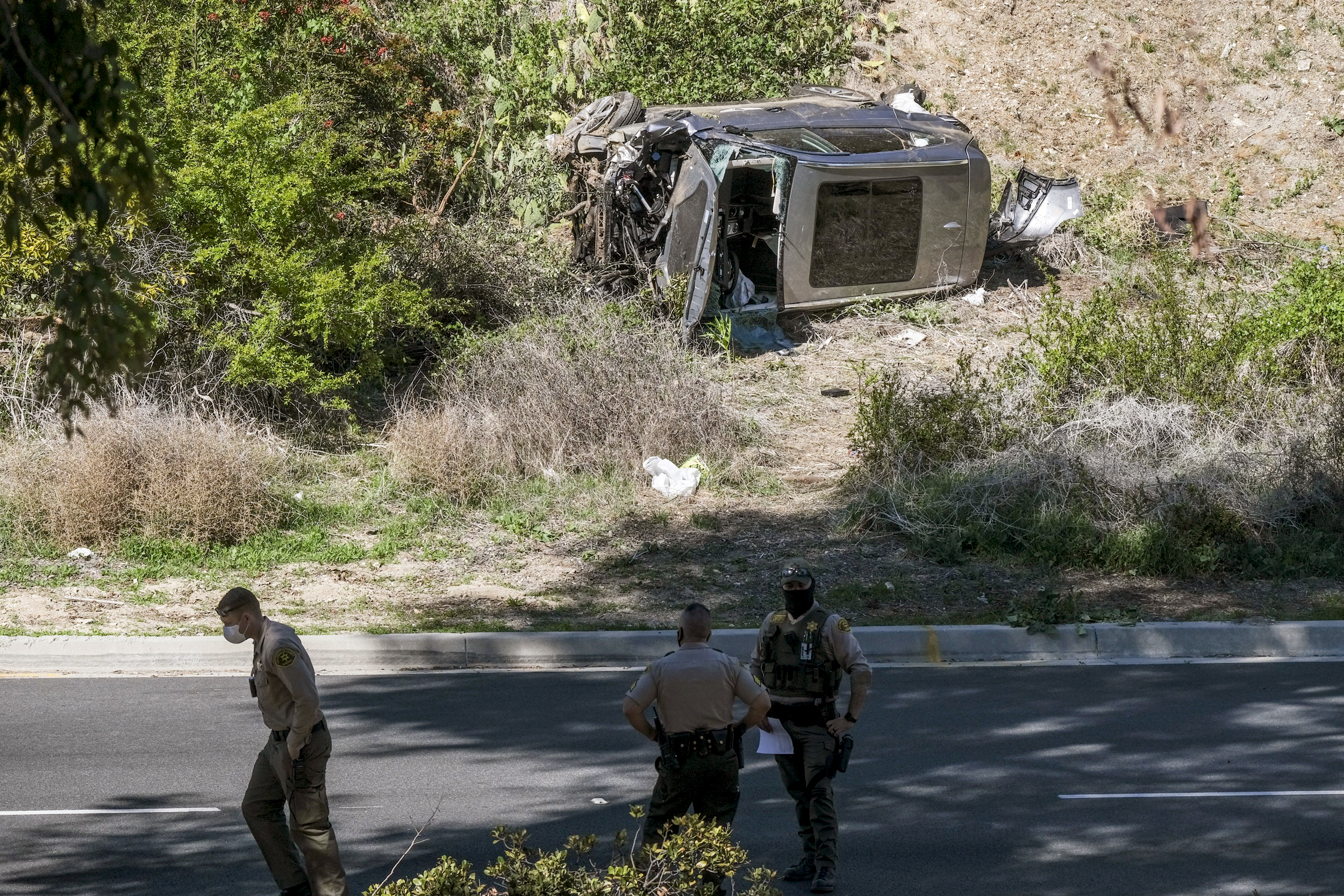 一个坐在路边的人：图片：2021年2月23日，涉及高尔夫球手Tiger Woods的翻车事故沿洛杉矶Rancho Palos Verdes区域的一条路，车辆停在其侧。（Ringo HW Chiu / AP）